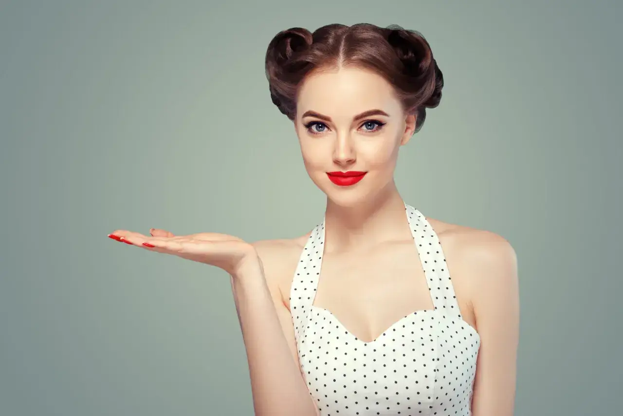 Kobieta w stylu pin up, z burzą loków i czerwoną szminką, prezentuje dłoń. To lata 50. w pełnej krasie.